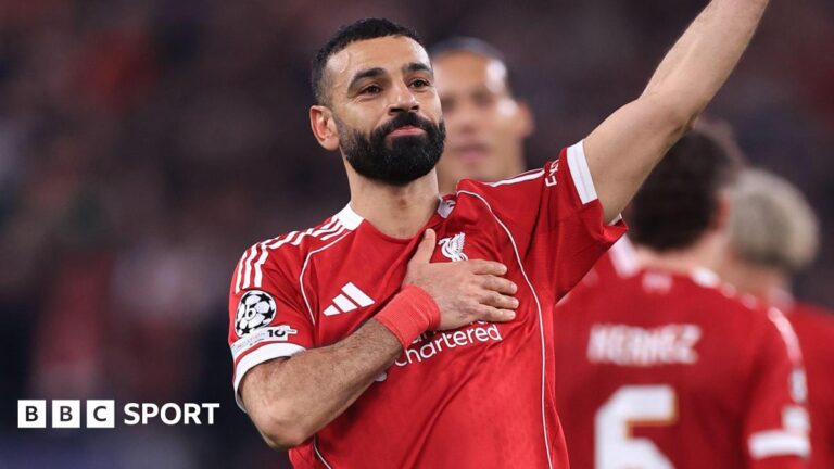 Liverpool forward Mohamed Salah waves to supporters with one hand while holding the Liverbird badge