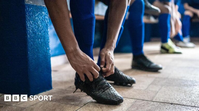 Soccer player tying shoelaces while preparing for match in the locker room