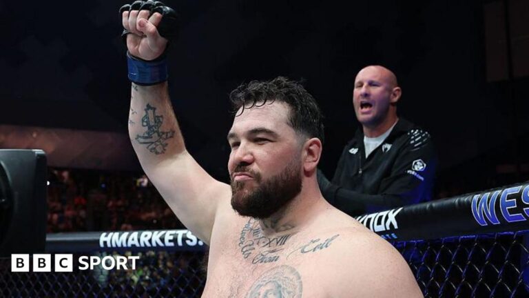 Louie Sutherland holds up his arm as he stands in the octagon