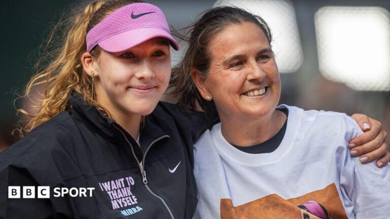 Mirra Andreeva puts an arm around Conchita Martinez as both smile. Andreeva is wearing a dark jacket that has the slogan 'I want to thank myself - Mirra'