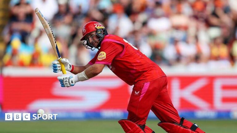 Joe Root, wearing red trousers, shirt and helmet, leans forward to play a shot with his bat held up in front of him