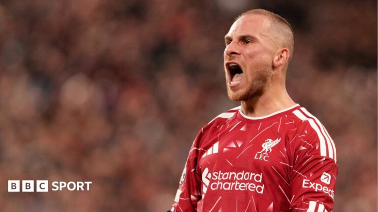 Liverpool 2-1 Atletico Madrid: Alexis Mac Allister does talking on pitch A man in a red jumper stands next to the 'THIS IS ANFIELD' sign which sits on a balck table.