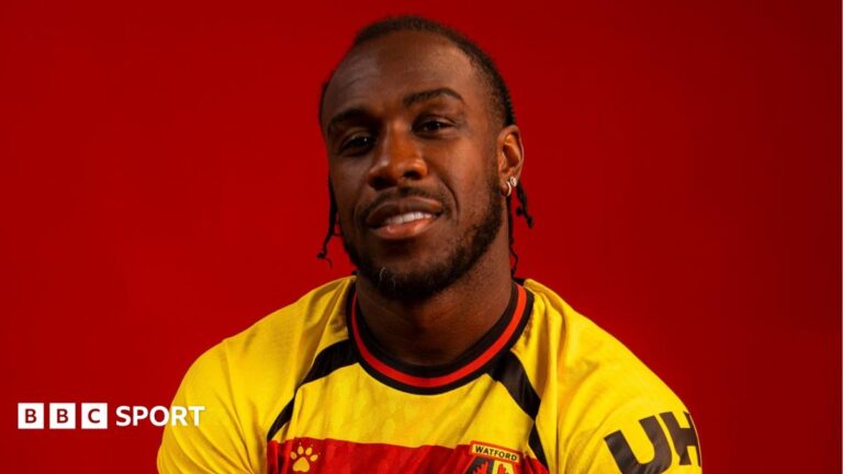 Michail Antonio poses in a yellow, red and black Watford FC jersey at a photocall.