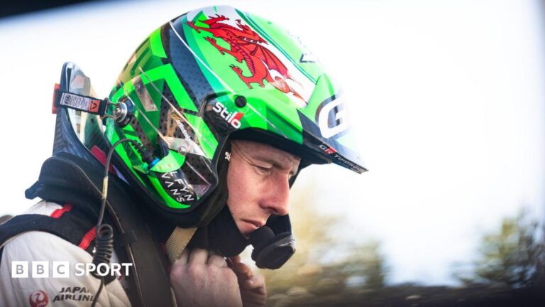 Elfyn Evans in a green and black helmet sporting a red Welsh dragon looks contemplative